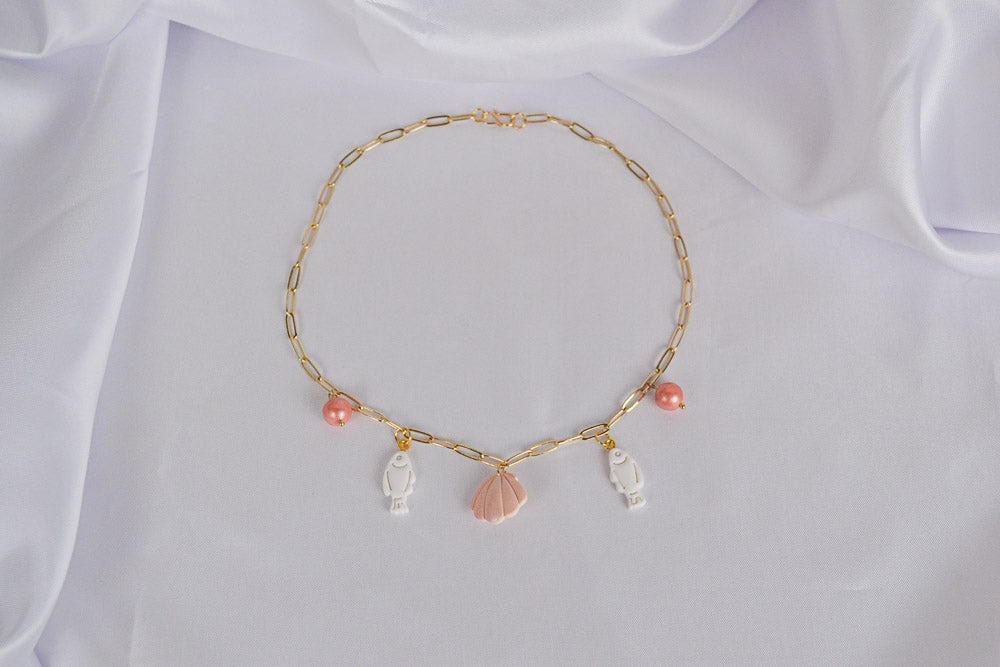 Charm Kette mit Fischen, Muschel und Perlen auf weißem Stoff