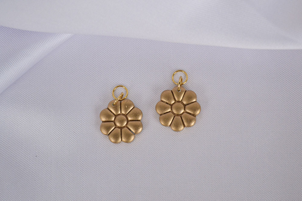 Zwei goldene Blumen Anhänger aus Polymer Ton auf einem weißen Tuch