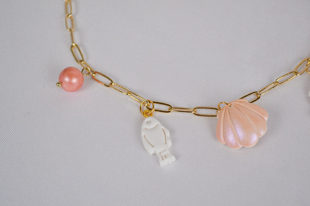 Weißer Fisch Anhänger einer Halskette, links eine Pinke Perle und rechts eine rosa / orange Muschel