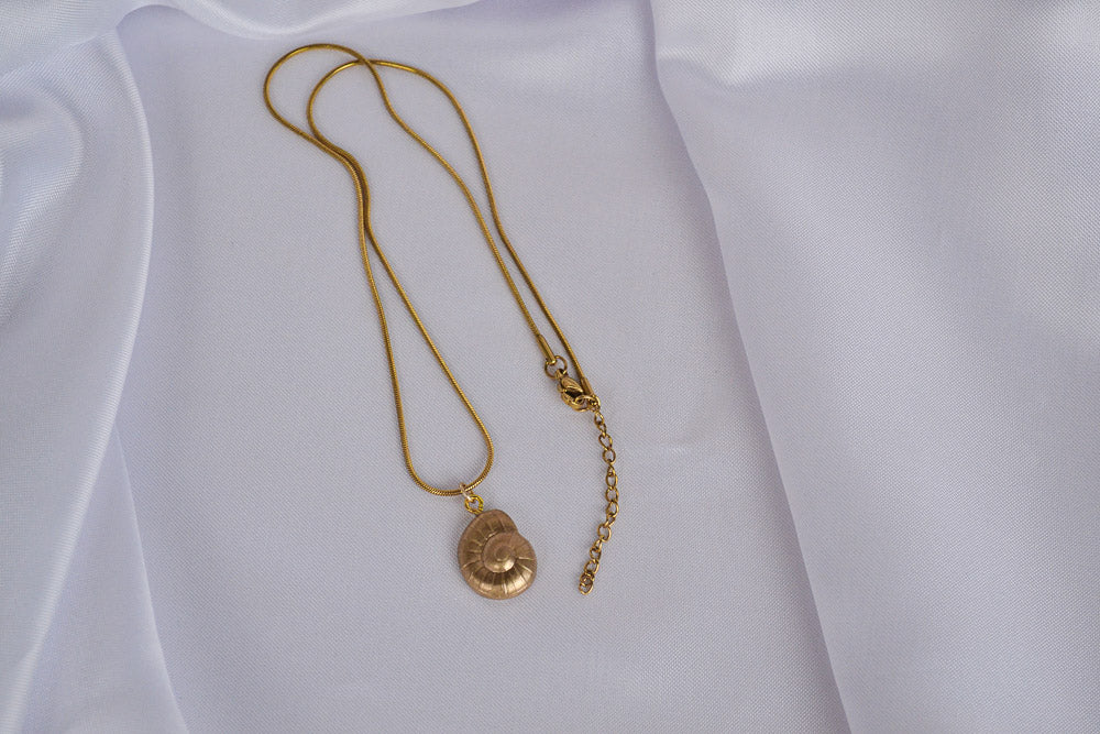 Halskette mit Muschel Charm in Gold auf weißem Stoff