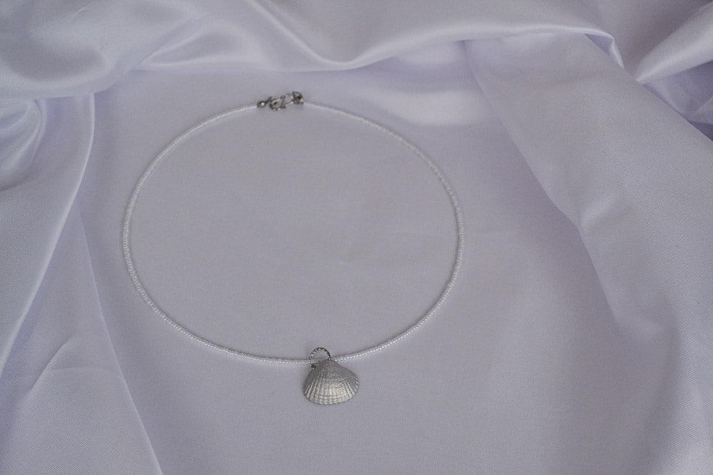 Perlenkette in weiß mit silber Muschel auf weißem Stoff