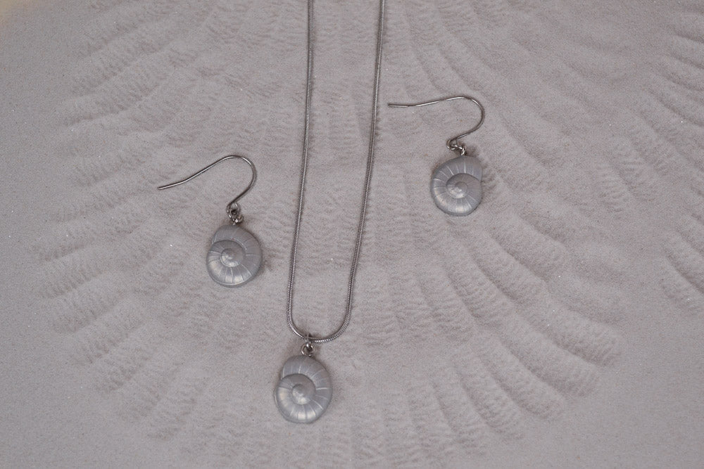 Schmuck Set aus einer Kette und Ohrringen mit silber Muschelanhängern auf Sand