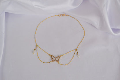Goldene Halskette mit Schmetterling und Perlen auf weißem Stoff