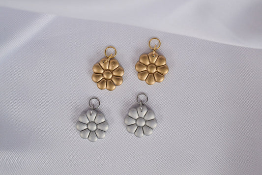 Zwei goldene Blumen Anhänger und zwei silber Blumen Anhänger auf einem weißen Tuch