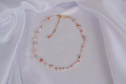 Ausgebreitete Edelsteinkette und Rosé und Orange auf einem weißen Tuch