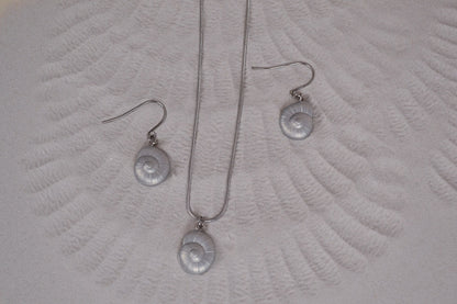 Schmuck Set aus einer Kette und Ohrringen mit silber Muschelanhängern auf Sand