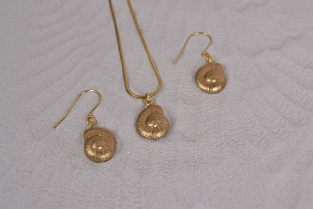 Goldene Muschel Charms an Ohrringen und einer Halskette auf Sand in Nahaufnahme