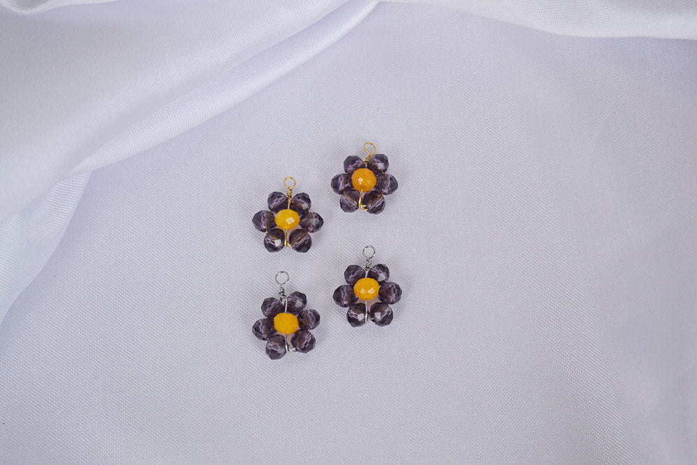 zwei Anhängern aus glänzenden Glasperlen in Violett und Gelb, handgemacht und geformt zu einer Blume